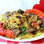 A plate of steak and lobster linguine with lobster tails and parsley