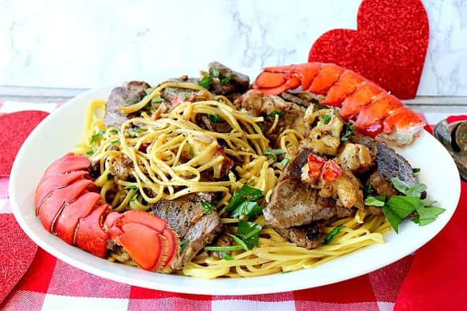 A plate of steak and lobster linguine with lobster tails and parsley