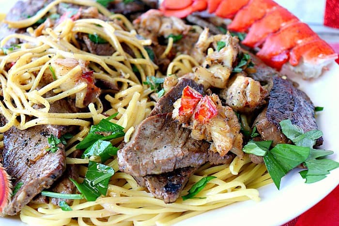 Closeup of surf and turf linguine on a plate with lobster tails and parsley.