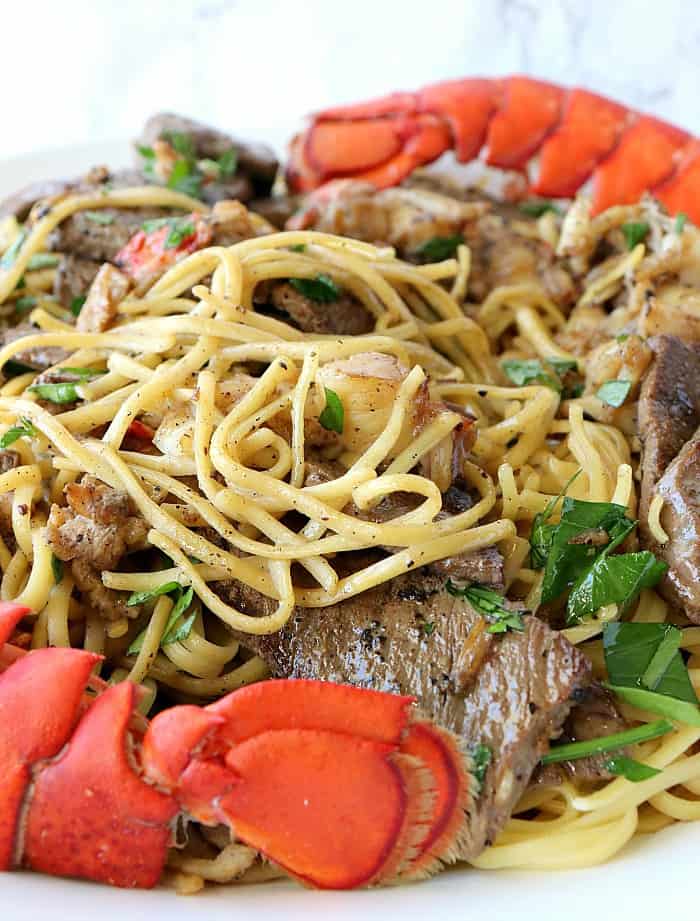 A closeup vertical image of linguine on a plate with lobster chunks and steak bites. A special occasion Valentine's dinner. Surf and turf pasta.