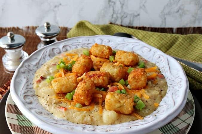 Tater Tot Chowder in a white filigree bowl with green onions and cheddar cheese.