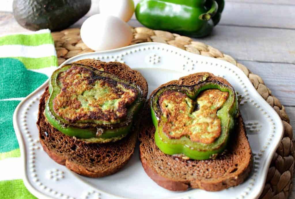 Two egg and avocado sandwiches stuffed into green pepper slices on a white plate.