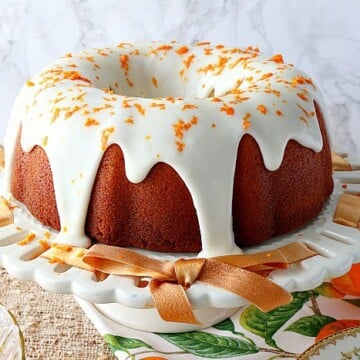 Citrus bundt cake with citrus icing and orange zest on a white cake plate.