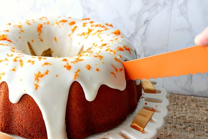 Orange knife cutting a slice of orange banana and poppy seed bundt cake.