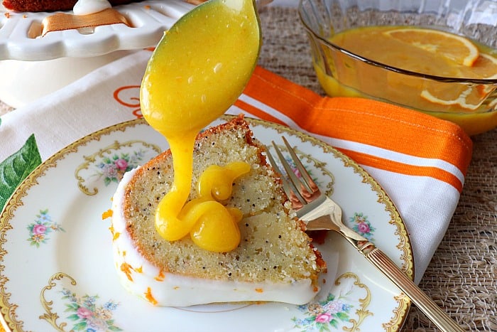 Fresh homemade orange curd being drizzled onto a slice of citrus bundt cake.