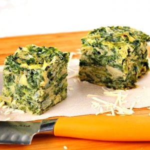 Two spinach artichoke squares on a wooden board with a knife in front.