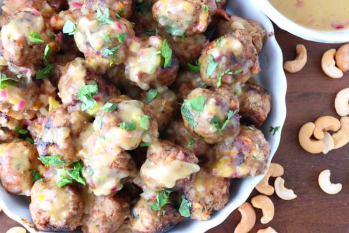 Closeup picture of turkey meatballs in a dish with sauce, chopped cilantro, and cashews on the side.