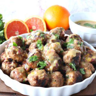 Turkey meatballs in a white dish with oranges and cilantro in the background