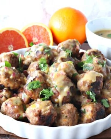 Turkey meatballs in a white dish with oranges and cilantro in the background
