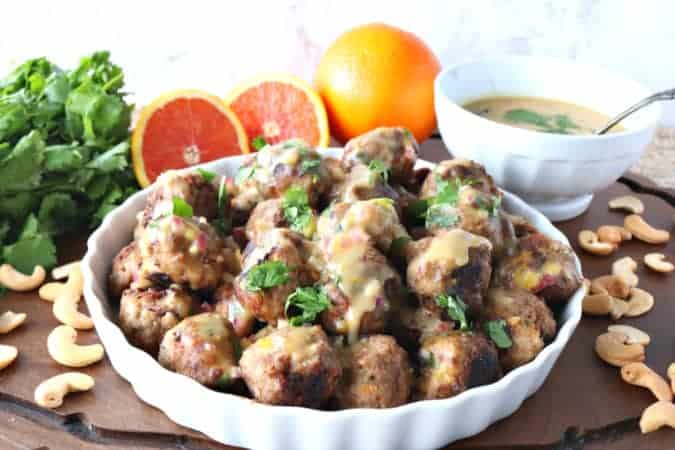 Turkey meatballs in a white dish with oranges and cilantro in the background