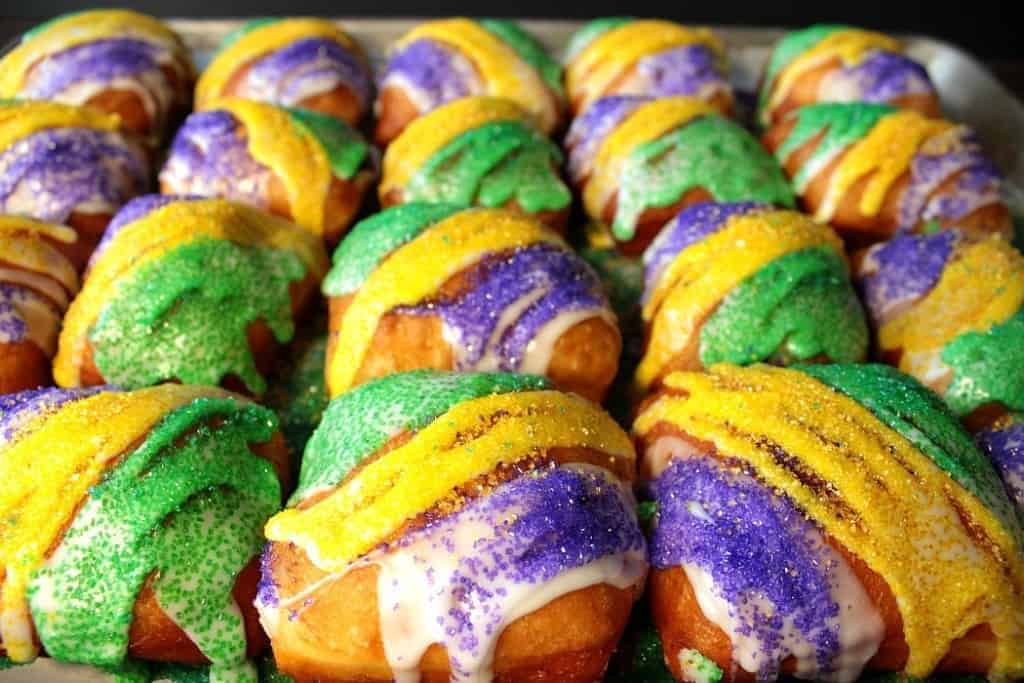 Tons of yellow, green, and purple sanding sugar fried beignets on a baking sheets.