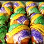 Tons of yellow, green, and purple sanding sugar fried beignets on a baking sheets.