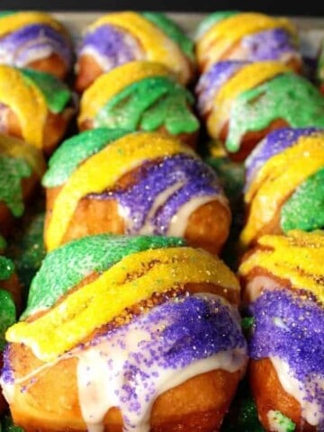 Tons of yellow, green, and purple sanding sugar fried beignets on a baking sheets.