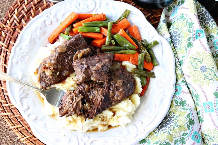 Overhead picture of braised short ribs on a white plate with carrots and green beans.