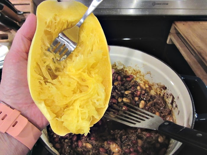 A hand holding a cooked spaghetti squash demonstrating how to remove the cooked strands with a fork,