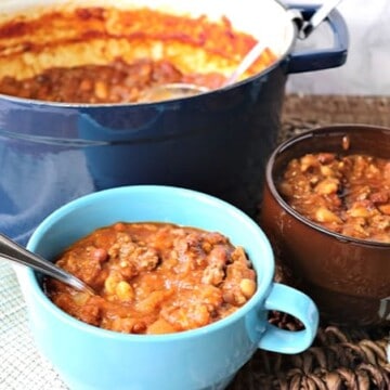 Two bowls of spaghetti squash chili in the foreground with a blue pot of chili in the background.