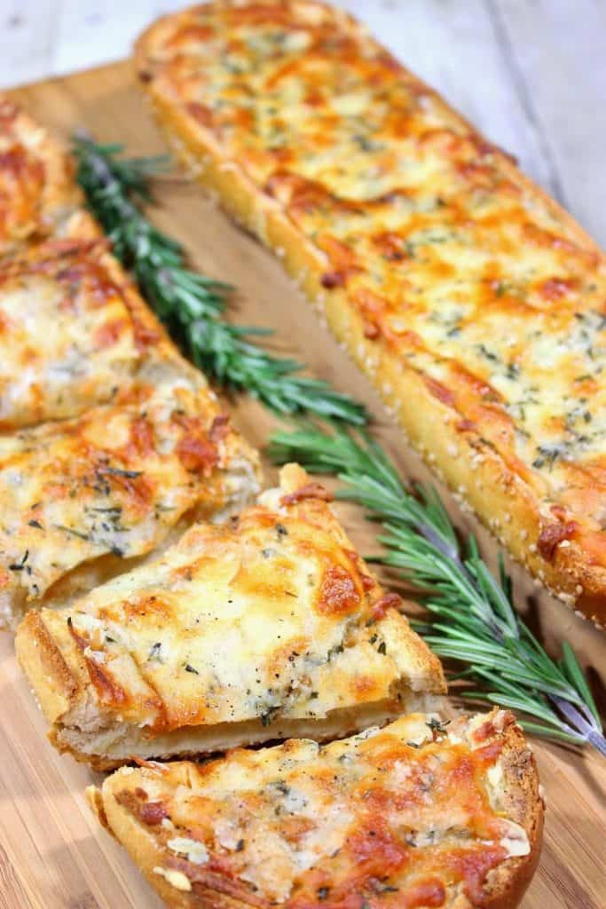 Two garlic cheese bread halves with rosemary sprigs on a cutting board.