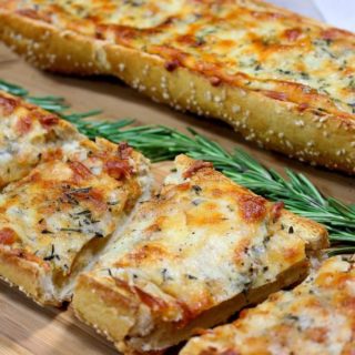Sliced garlic cheese bread with rosemary spears on a cutting board.