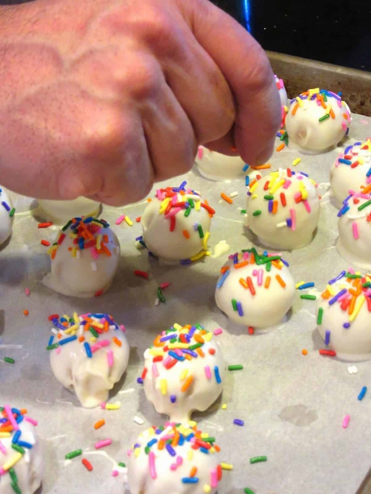 A hand putting sprinkles on a No-Bake Shortbread Cookie Truffle.