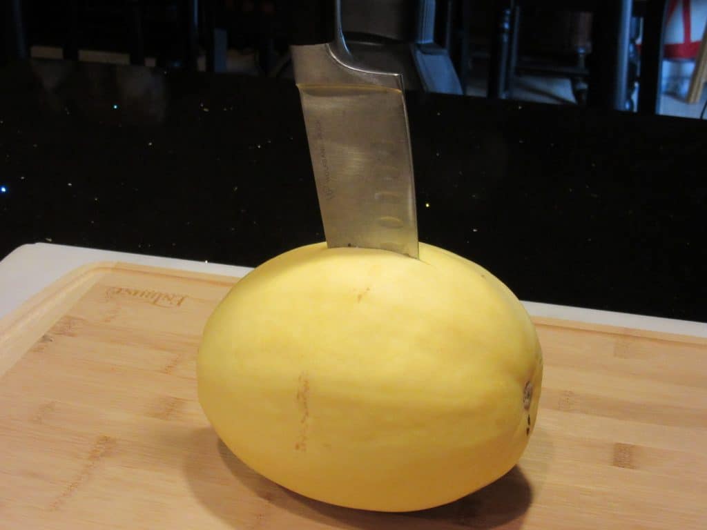 Spaghetti squash with a chef's knife inserted in the center.