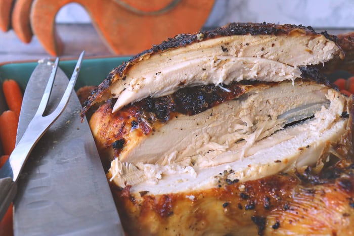 Closeup of a sliced breast of an air fryer whole chicken with a knife and a carving fork.