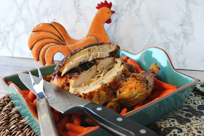 Sliced Air Fryer Whole Chicken with a carving knife and fork resting on the baking dish.