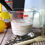 Buttermilk alternative inside a measuring cup with a lemon, apple cider, milk, spoons and a whisk surrounding it.