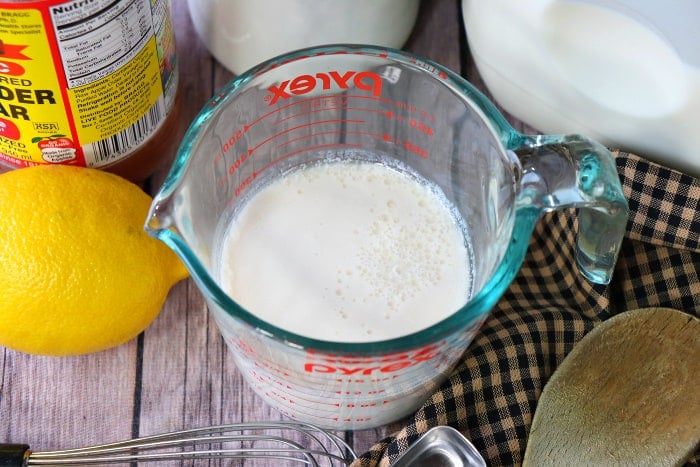 Overhead picture of buttermilk in a measuring cup with a whisk, measuring spoon, and wooden spoon in the foreground. 