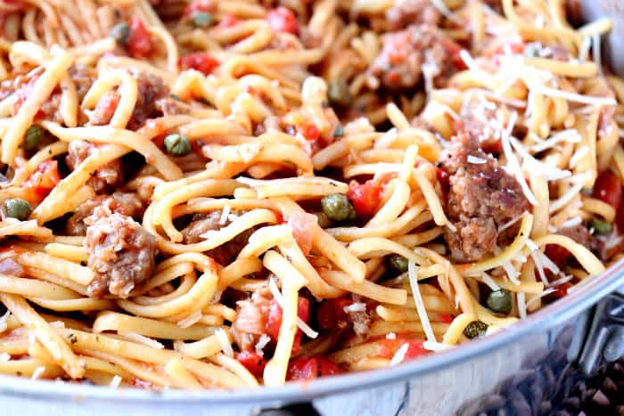 Closeup photo of linguine pasta with sausage, tomatoes, capers, and shredded Parmesan cheese.