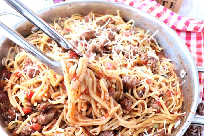 A pot of linguine pasta with tongs and a red and white check napkin.