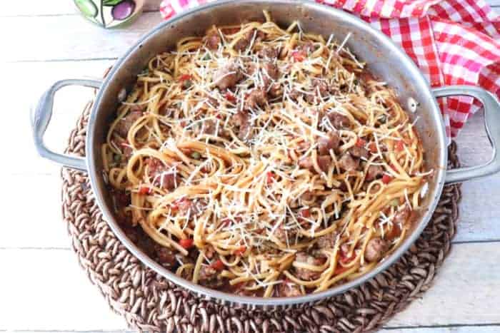 Overhead photo of a pan filled with pasta, sausage, and cheese with a red and white checked napkin.