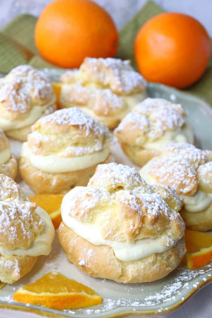 Vertical picture of a plate of orange eclairs with orange whipped cream. Valentine's dinner recipe roundup.