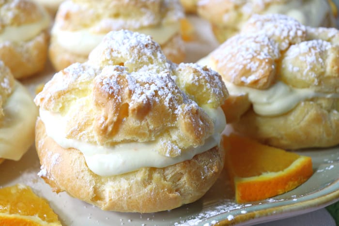 Closeup of profiterole filled with orange curd whipped cream and a confectioners sugar dusting