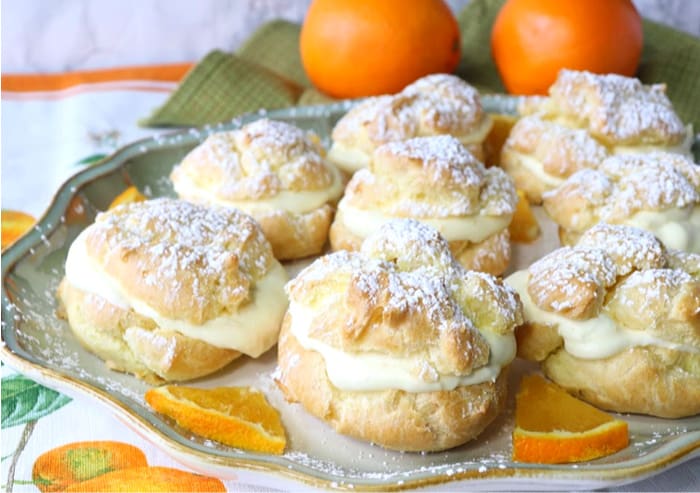 Golden filled eclairs on a plate with oranges and confectioners sugar