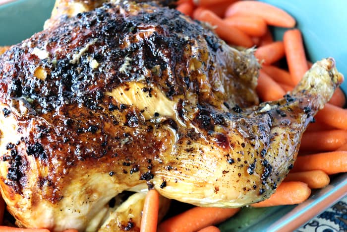 Closeup of browned, whole chicken in a blue baking dish with carrots.