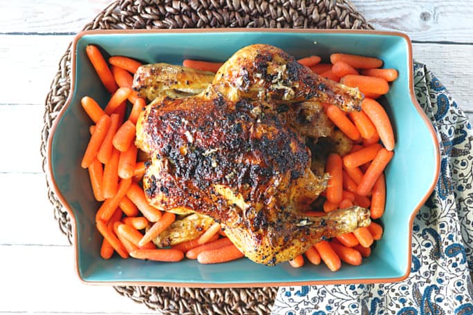 Overhead picture of a whole chicken in a blue baking dish with carrots.