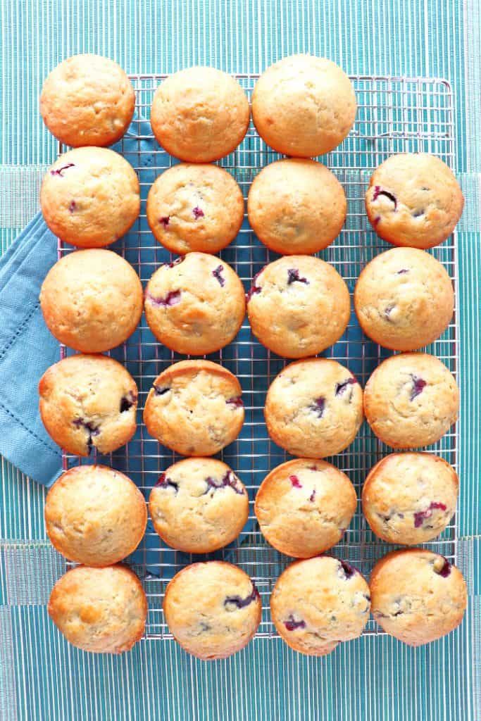 Overhead picture of 23 golden brown muffins on a cooling rack with a blue napkin.