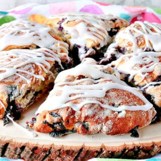 A sliced wooden board filled with Blueberry Lemon Scones and along with an icing drizzle.