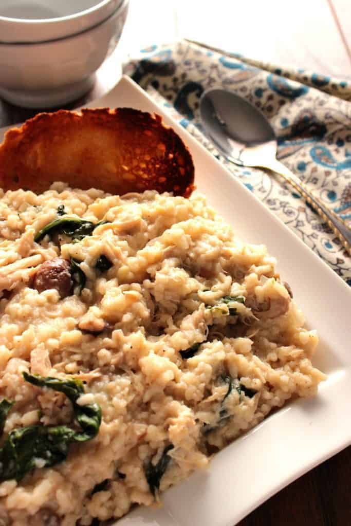 Risotto with mushrooms and spinach on a white square plate and a slice of toasted bread.