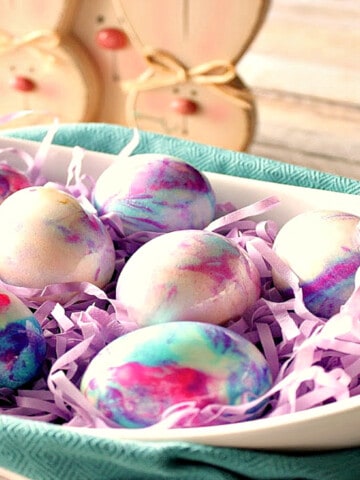 An oval white bowl filled with pastel colored Tie-Dye Easter Eggs.