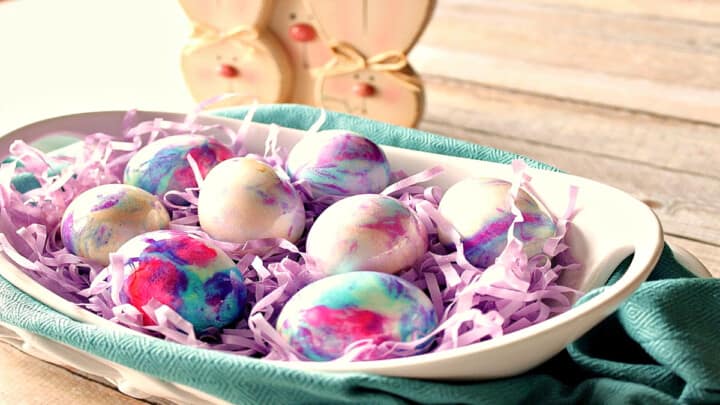 An oval white bowl filled with pastel colored Tie-Dye Easter Eggs.