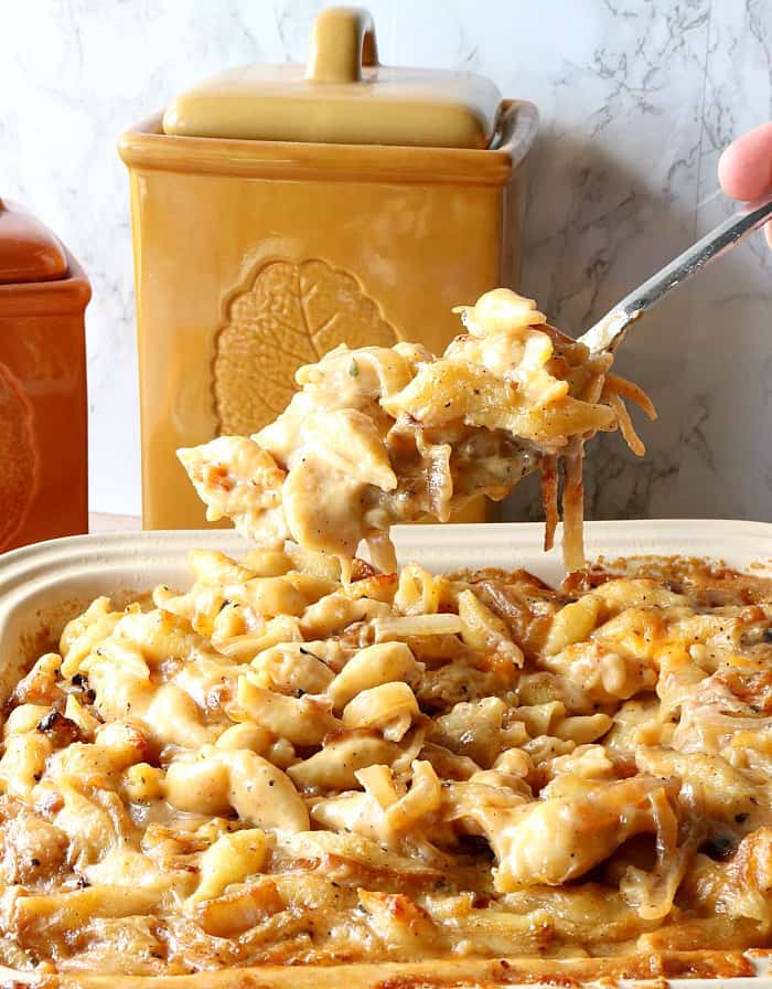 Vertical photo of a spoonful of french onion macaroni and cheese with canisters in the background.