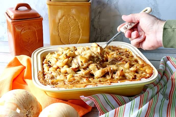 Hand with a spoon serving up French onion mac and cheese out of a casserole dish. Popular Thanksgiving side dish recipe roundup.