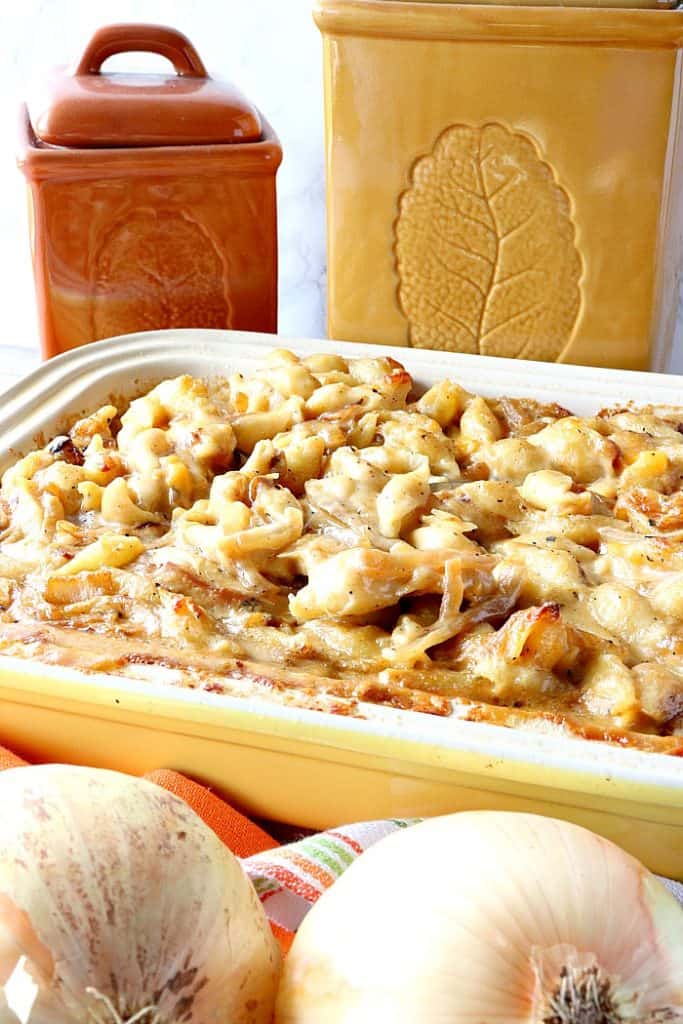Vertical image of baked mac and cheese in a casserole dish with onions in the foreground and canisters in the background. 