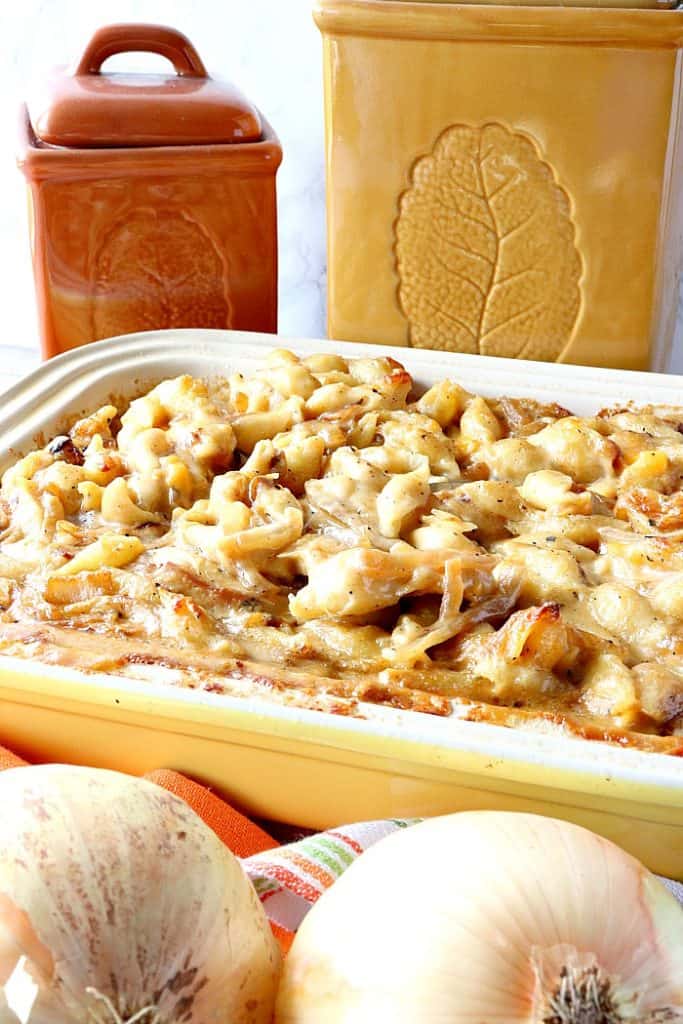 Vertical image of baked mac and cheese in a casserole dish with onions in the foreground and canisters in the background.