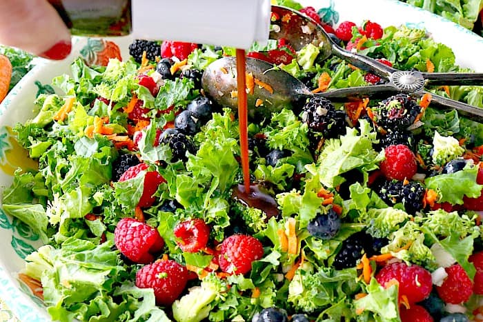 Homemade vinaigrette being poured on a colorful kale salad.