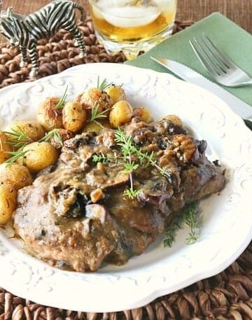 Steak with bourbon mushroom sauce on a white plate with baby potatoes and fresh herbs.