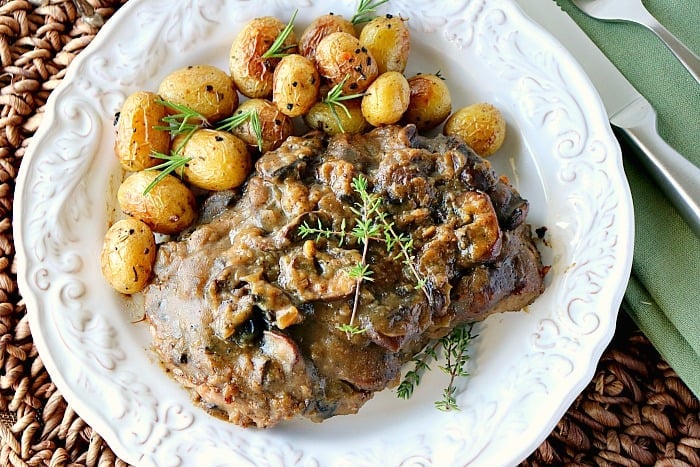 Overhead photo of a strip steak with bourbon mushroom sauce on a white plate with baby new potatoes and fresh herbs.