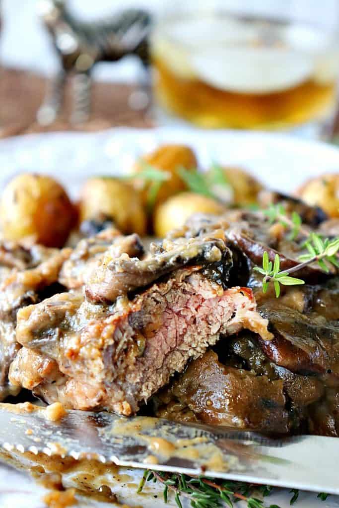 Sliced Steak on a plate with potatoes in the background and fresh thyme garnish.