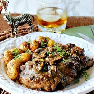 Steak with Bourbon Mushroom Sauce on a white plate with a glass of bourbon with ice in the background.